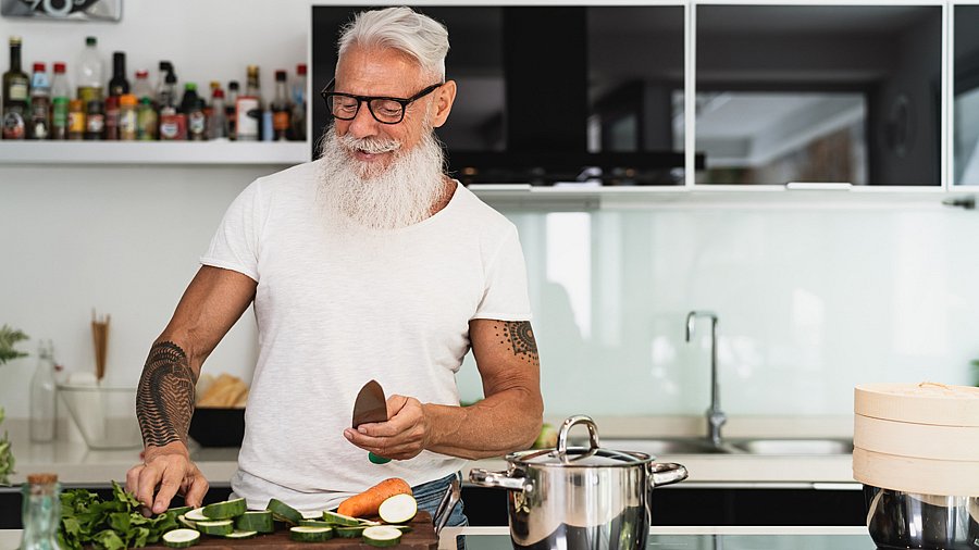 Tätowierter Mann steht in einer Küche und schneidet Gemüse