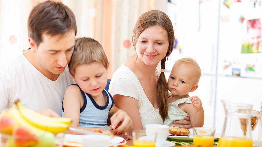 Junge Eltern beim gemeinsamen Frühstück mit zwei Kleinkindern.