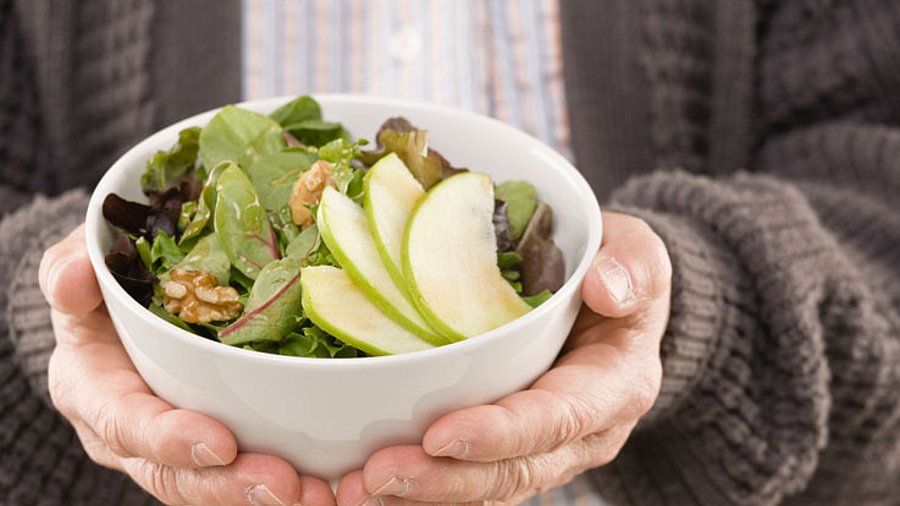 Ältere Mann (Kopf ist nicht zu sehen) hält eine Schale Salat mit Nüssen.