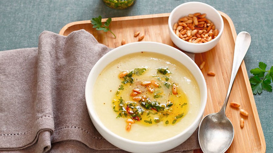 Eine weiße Schale mit Suppe. Serviert mit Kräutern und Pinienkerne.