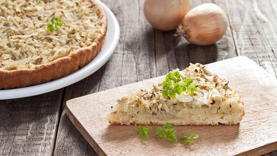 1 Stück Zwiebelstück, im Hintergrund ein ganzer Kuchen mit zwei Zwiebeln dekoriert.