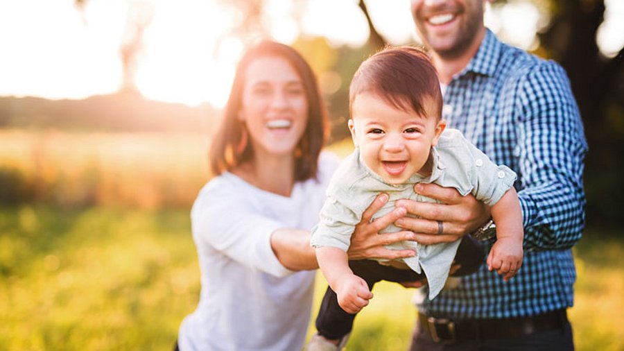 Mutter und Vater heben ein Kleinkind zusammen in die Luft.